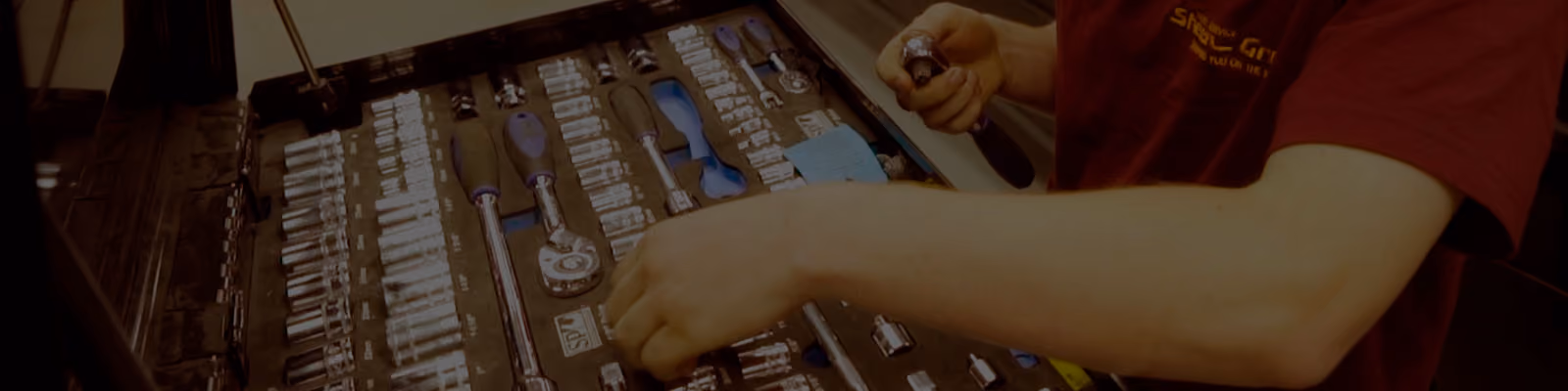 Person in red shirt selecting a socket wrench from a socket set organized in a black case.