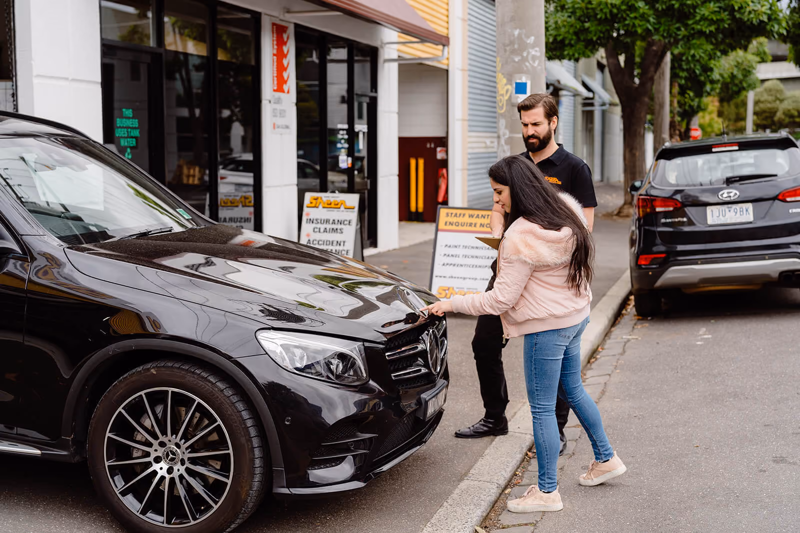 Woman showing a Sheen expert the damaged caused to her black car.