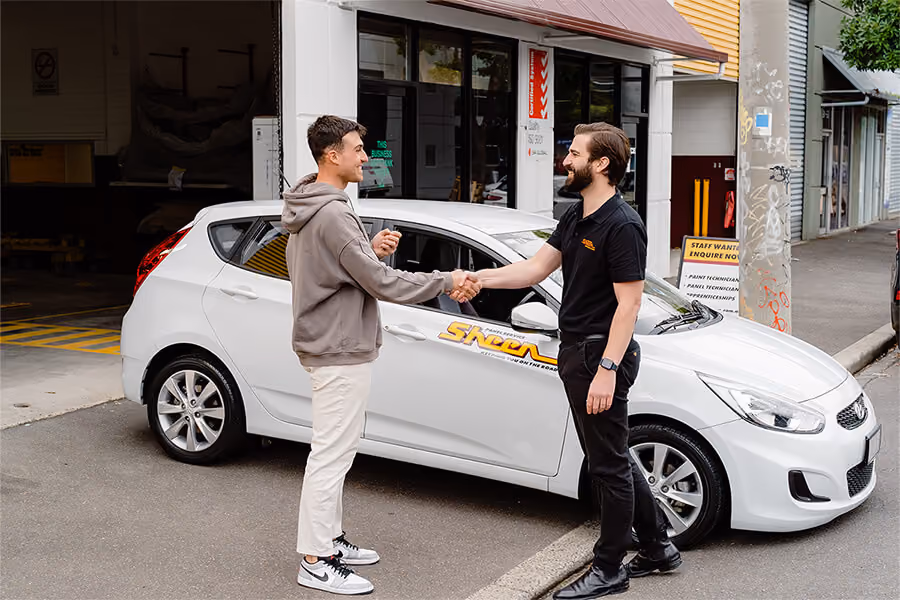 Sheen worker and customer shaking hands, customer is getting a temporary Sheen vehicle.
