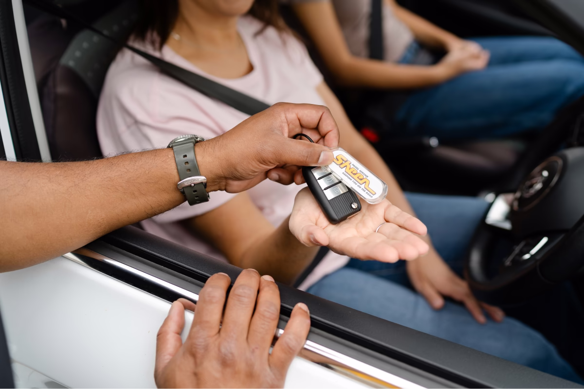 Woman in a white replacement car getting keys from a Sheen worker.
