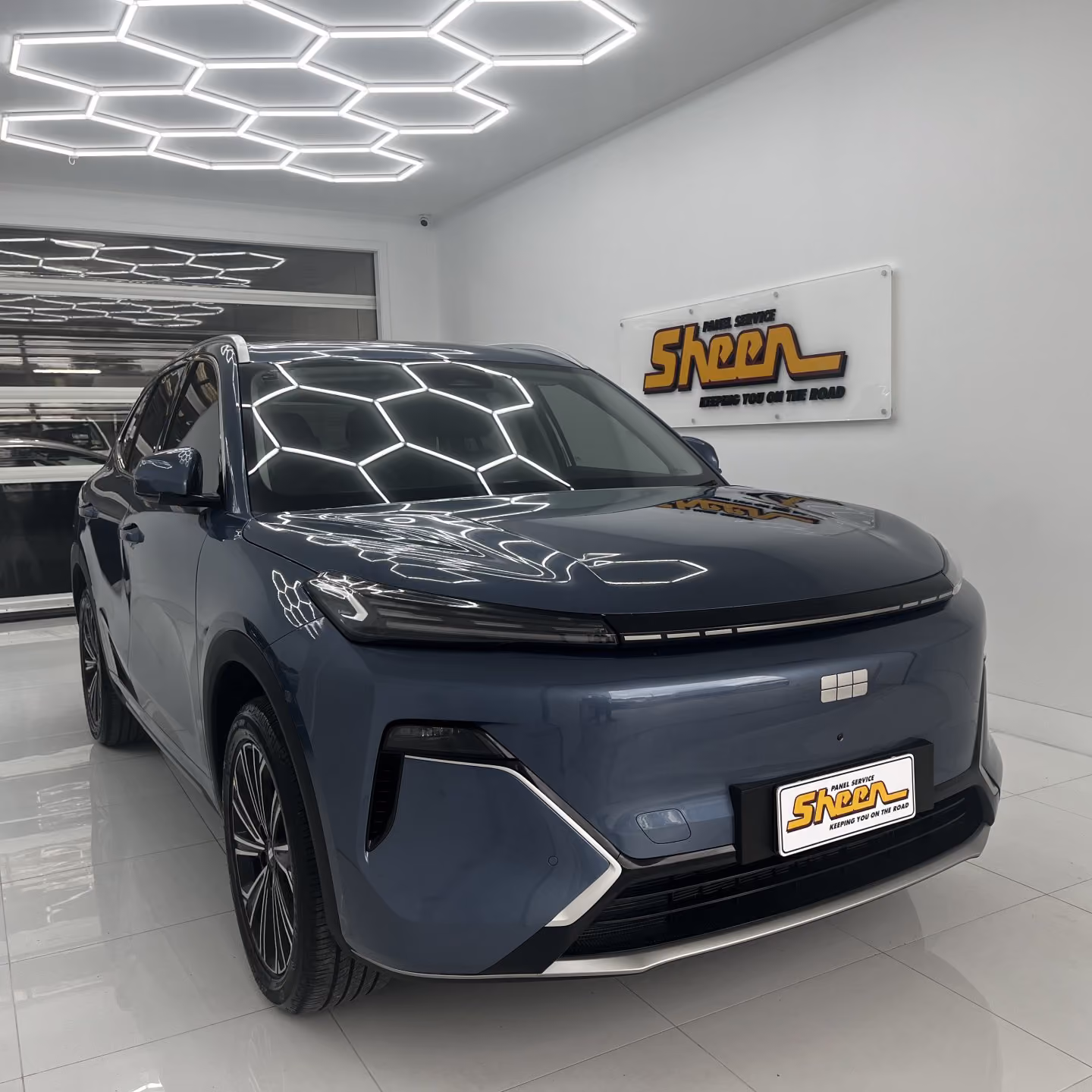 Geely electric SUV with front-end collision damage outside Sheen Panel Service workshop.