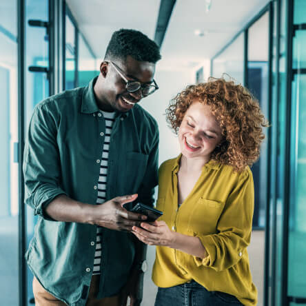 Two happy colleagues looking at a phone, meant to represent the positive results of an employee reward program.