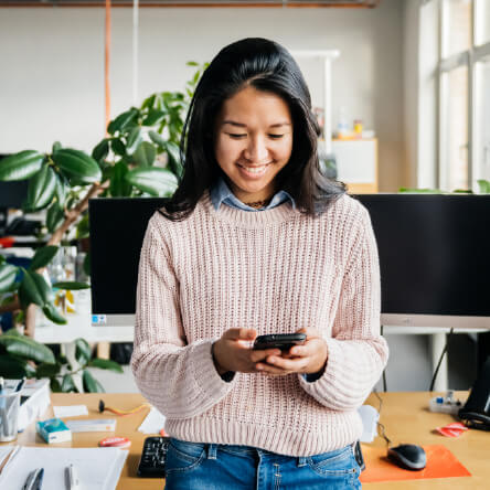 A woman in an office looking happily at her phone, meant to represent the power of sales incentive ideas for sales teams.