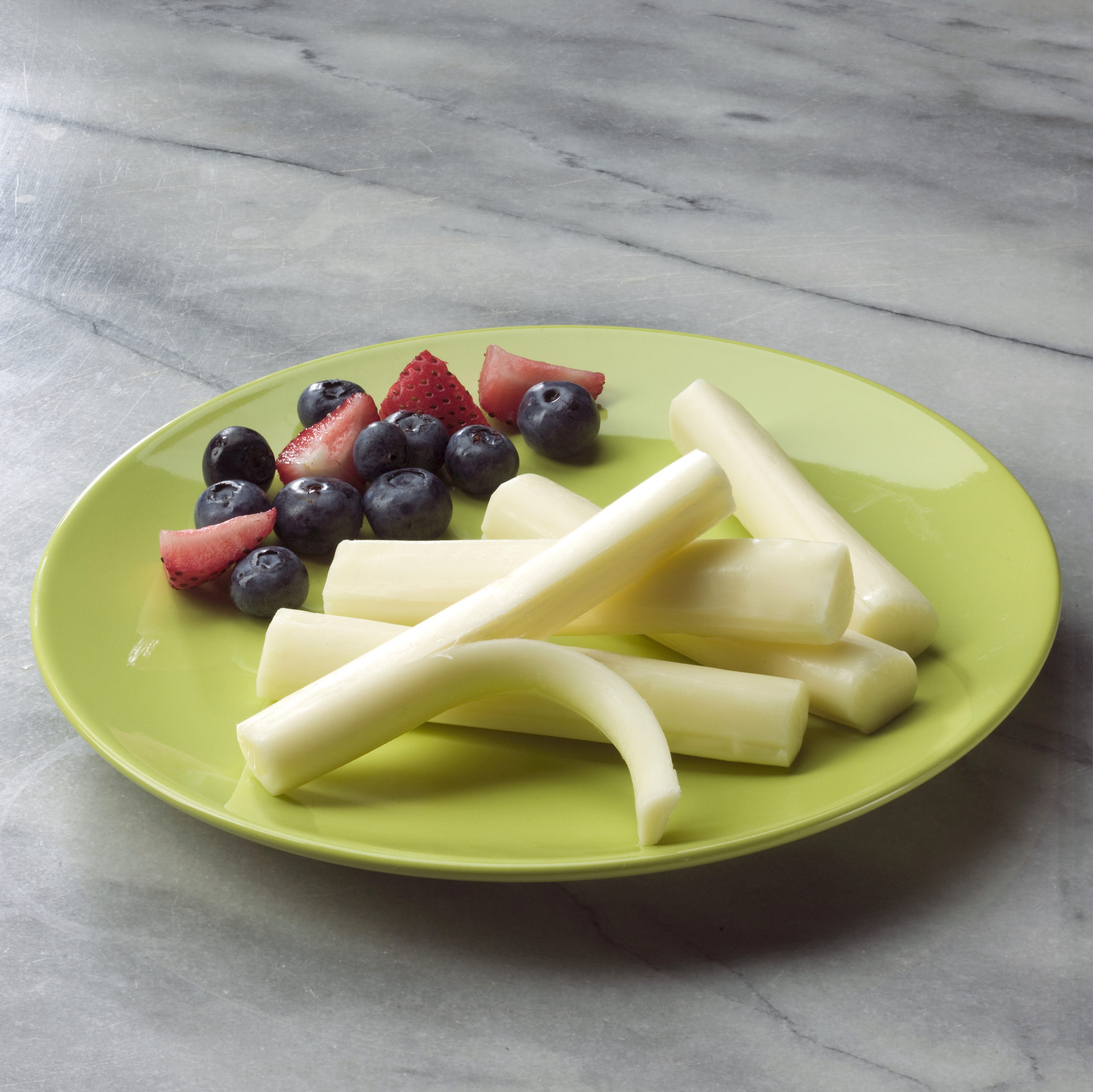 A green plate of Miceli's Mozzarella String Cheese garnished with fresh fruit