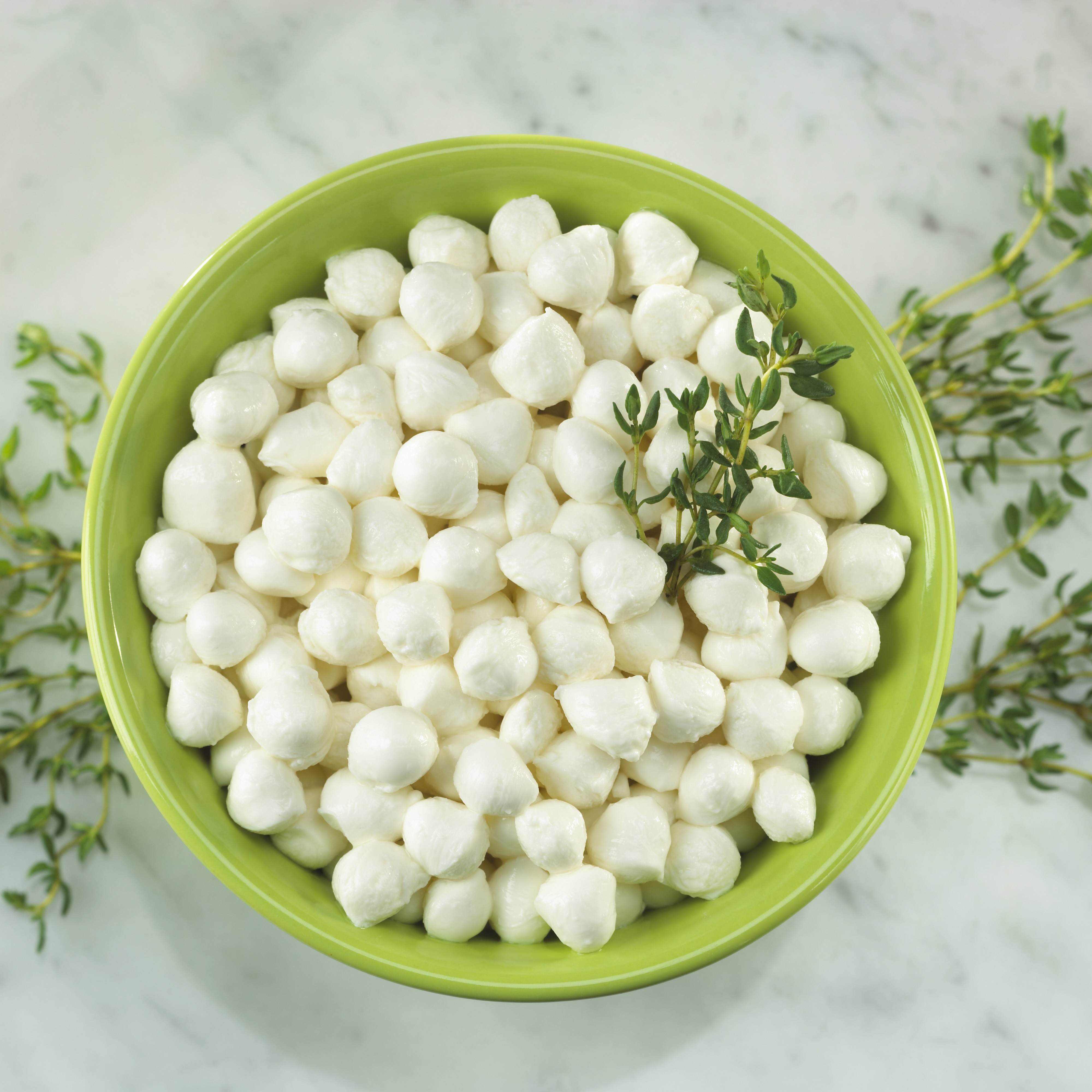 A green bowl of Miceli's Fresh Mozzarella Perline garnished with fresh herbs