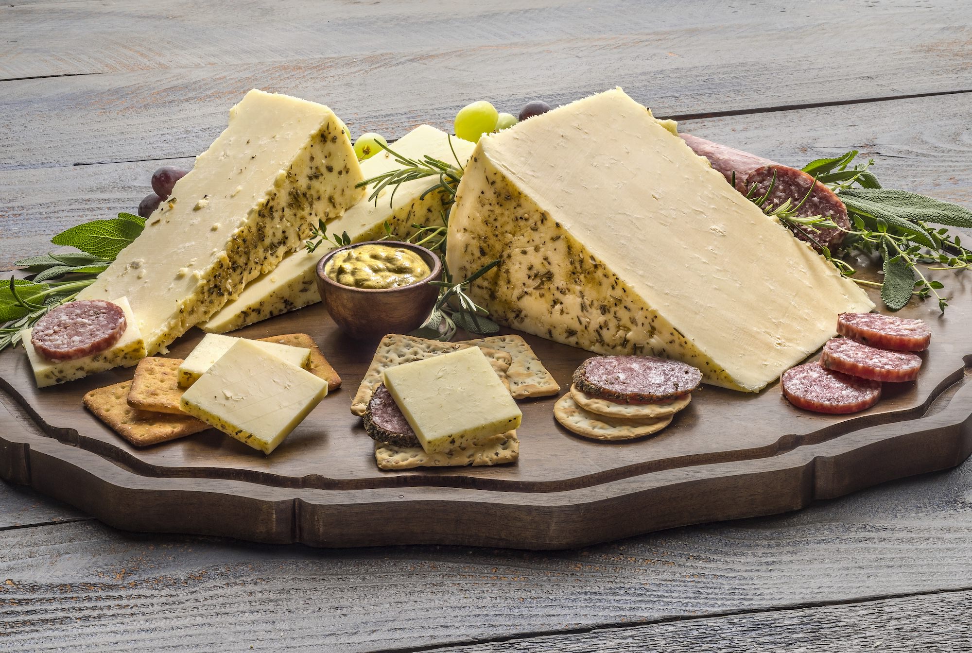 Mustard and herb rubbed cheddar displayed on a charcuterie board.