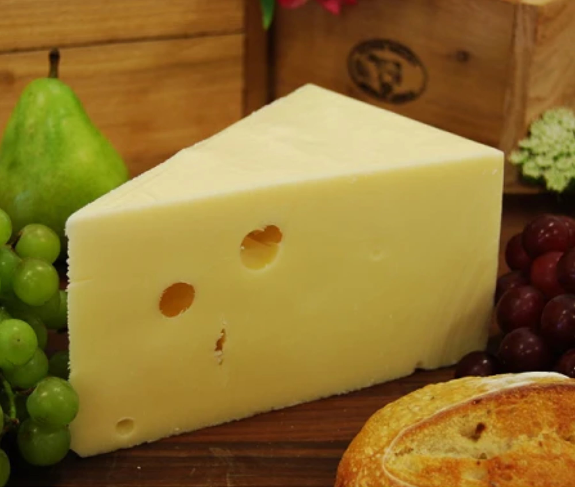 A wedge of swiss cheese surrounded by fresh bread and fruit. 
