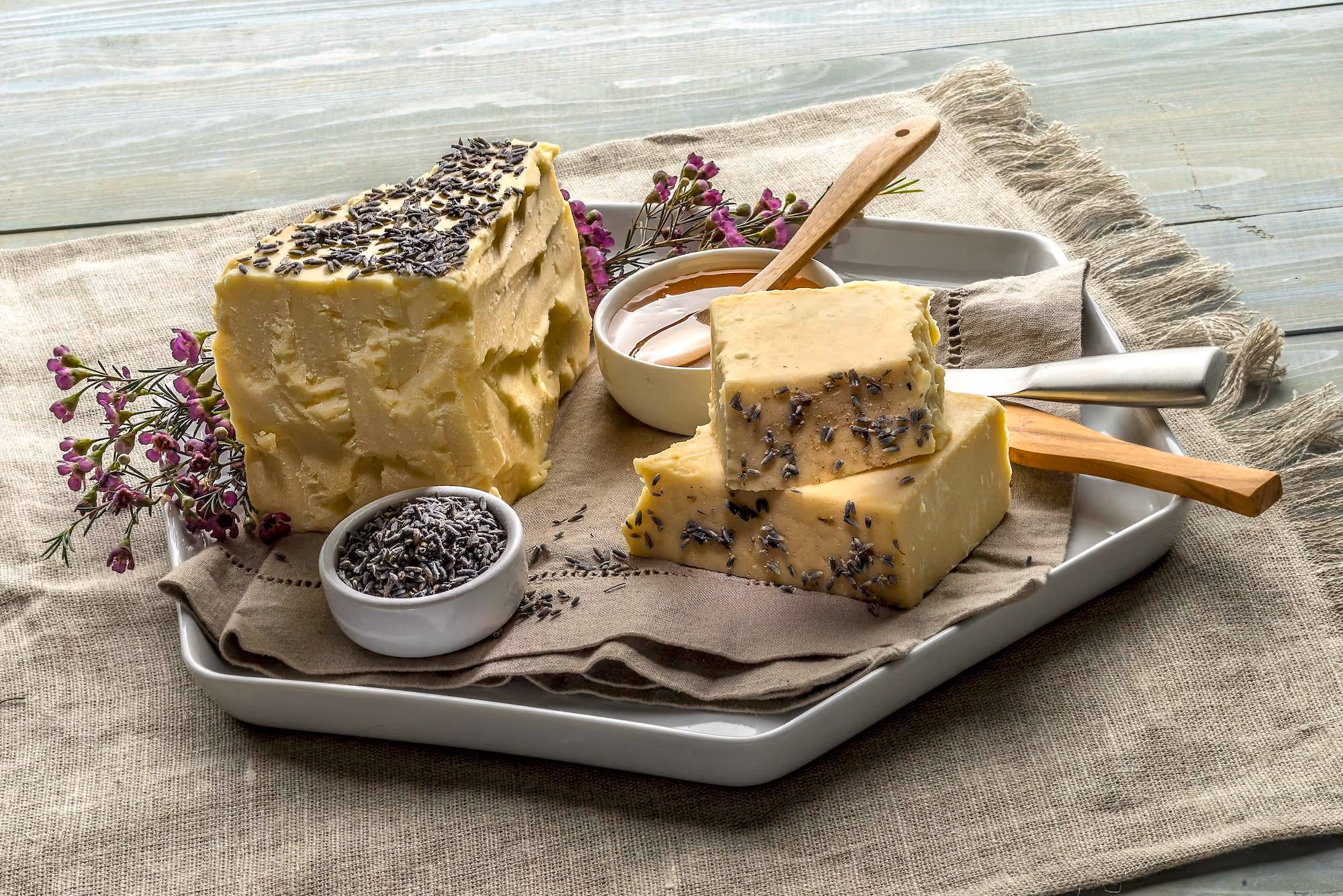 Fresh wedges of white cheddar on a white plate with fresh honey and lavender. 