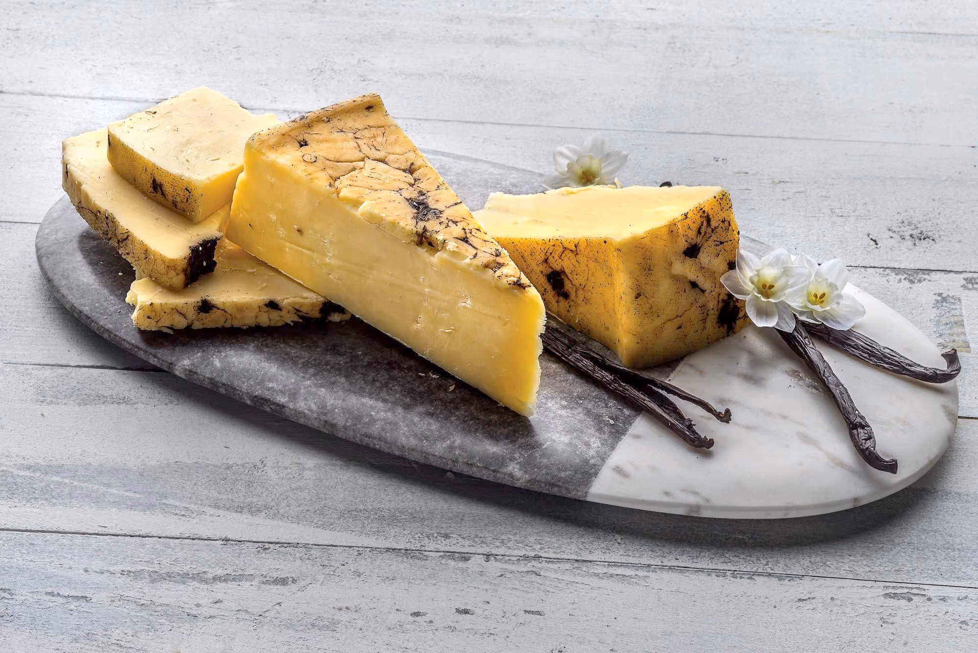Fresh cheddar rubbed with tahitian vanilla bean on a stone cutting board. 