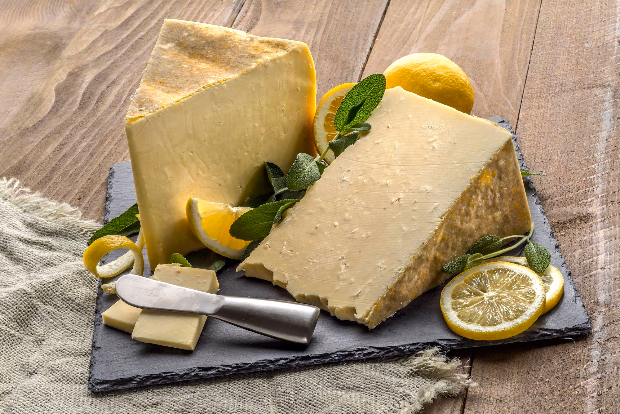 Wedges of Holstein white cheddar on a stone board with fresh sage and lemons.