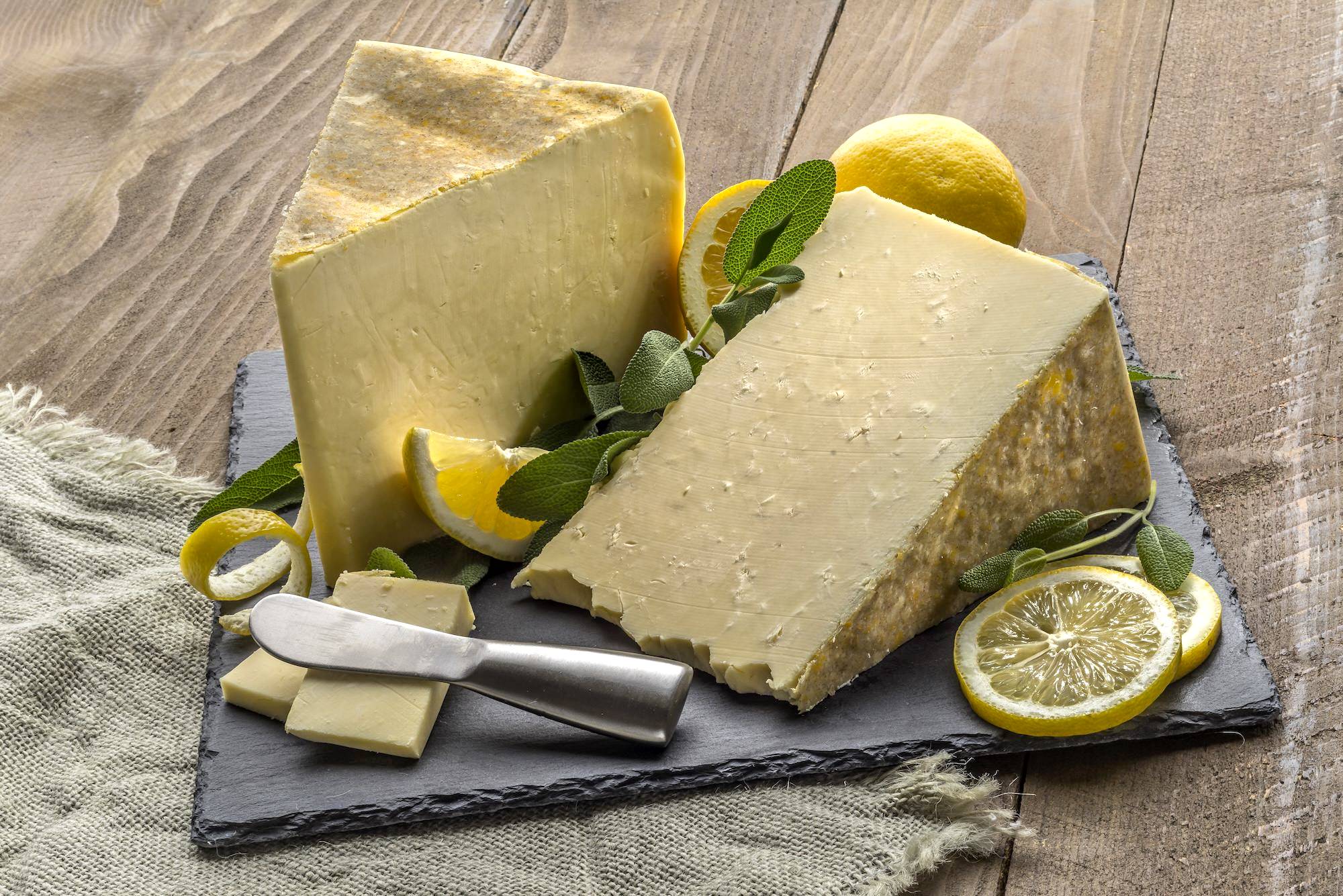 Wedges of Holstein white cheddar on a stone board with fresh sage and lemons.