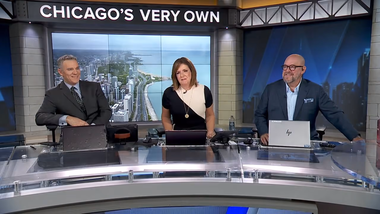 Chicago's Very Own WGN9 Newsroom - showing a male, female, and male news anchors at a news desk. The each have a laptop and the Chicago skyline is seen on a digital screen behind them.