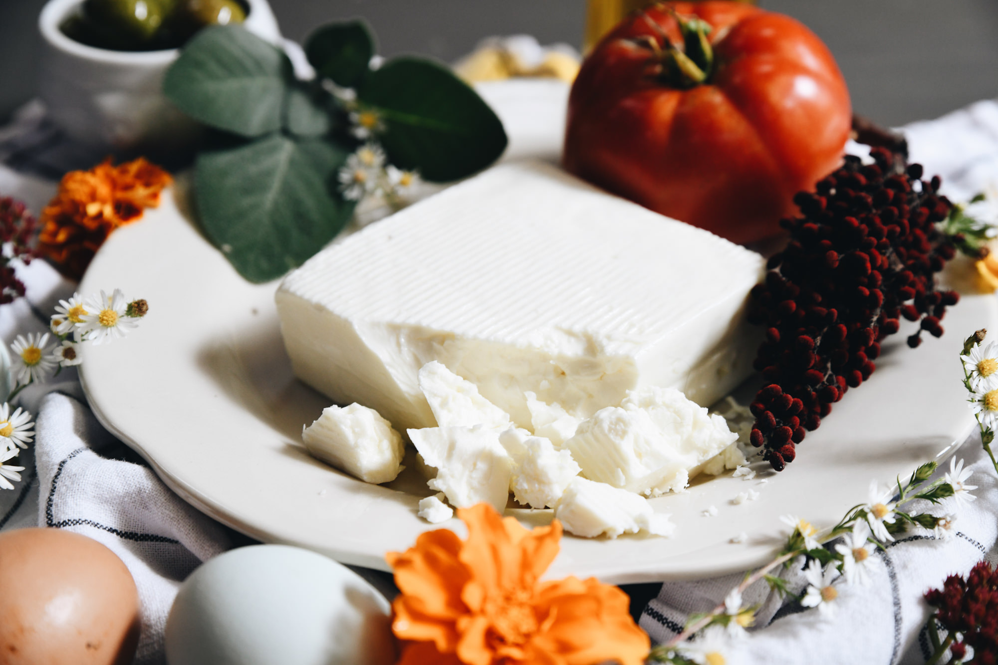 An image of a block of Green Dirt Farm Sheep's Milk Feta surrounded by vegetables, flowers and greens