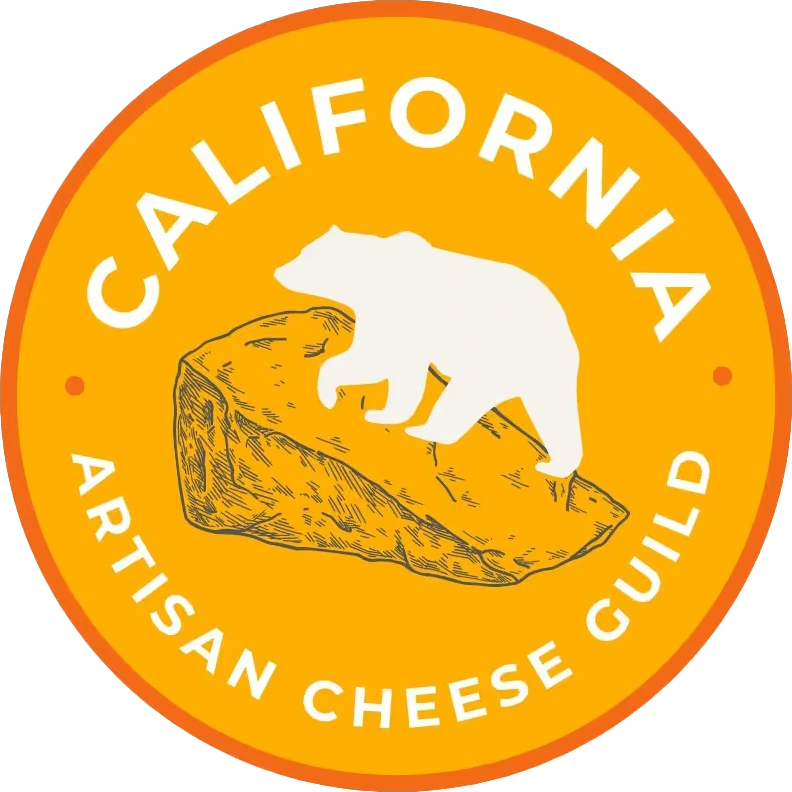 Logo for the California Artisan Cheese Guild: a white bear silhouette on a hand-drawn wedge of cheese inside a golden-orange circular badge, with the guild name wrapping around the edge in white capitals.