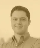 Portrait of a young man with short dark hair wearing a collared shirt, smiling slightly against a plain background.