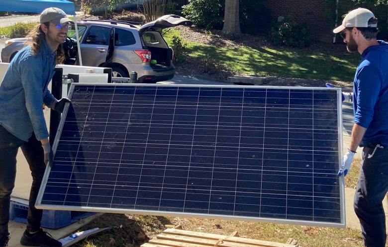 Two workers carry a solar panel