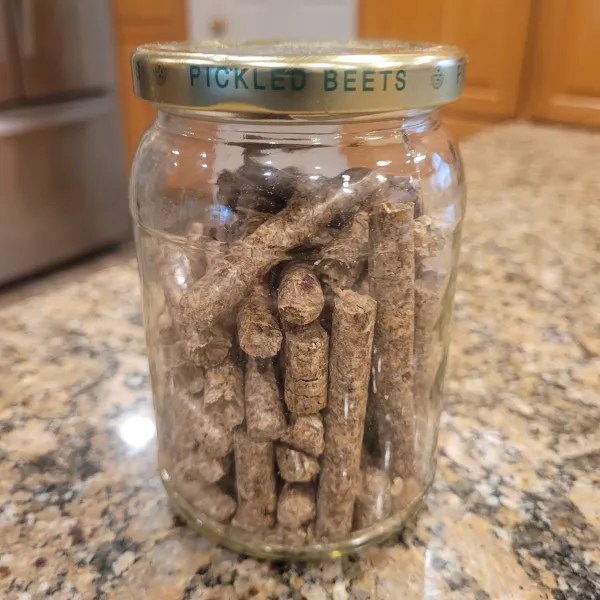 A jar with "pickled beets" on the lid with long, cylindrical wood pellets inside.