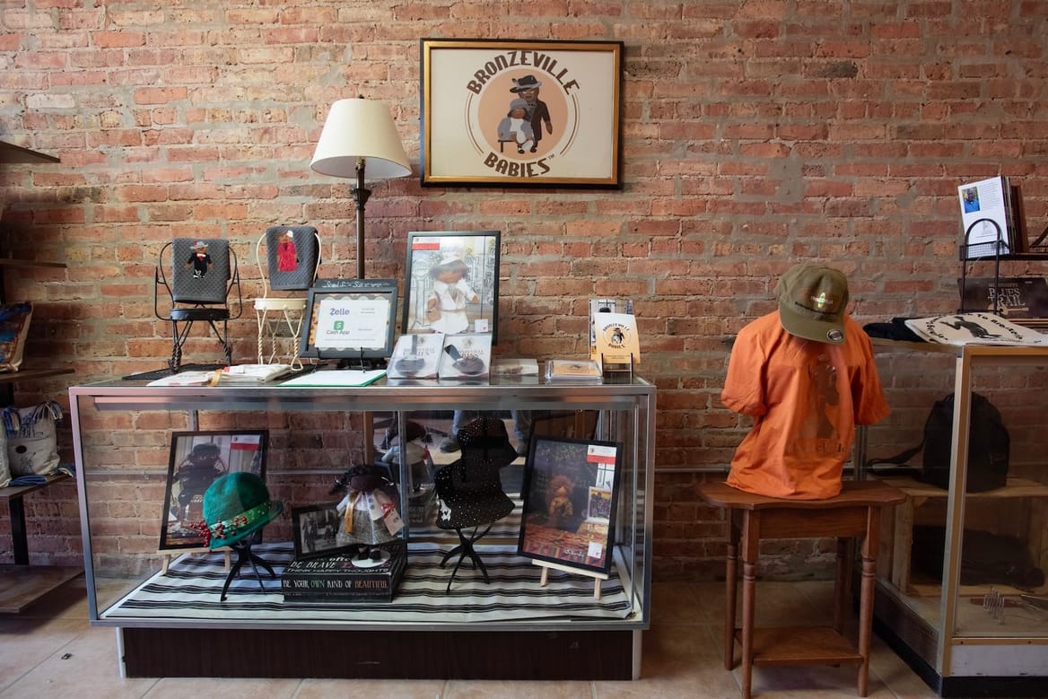 Framed images, a shirt and hat, and other items on shelving units in front of a brick wall.