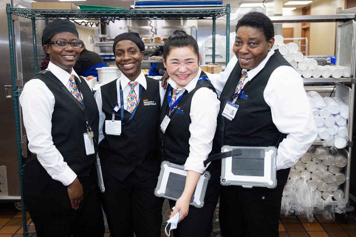 Four people in uniforms smiling and holding iPads.