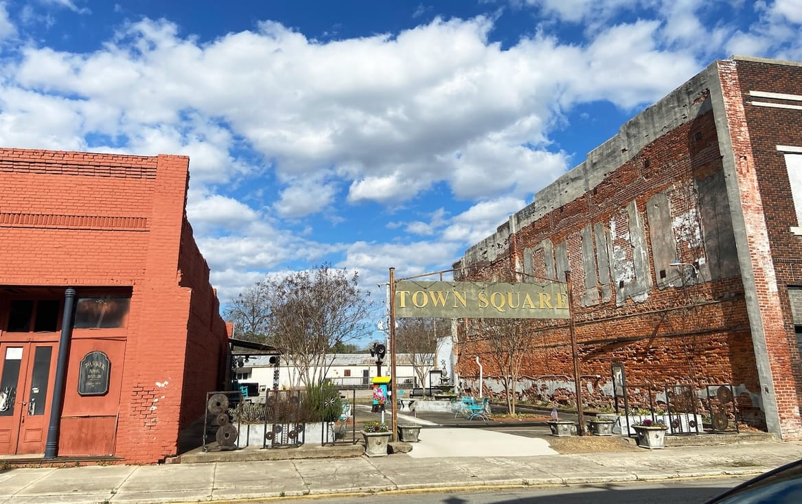 A sign reading "Town Square" at the entrance to a space between two brick buildings.