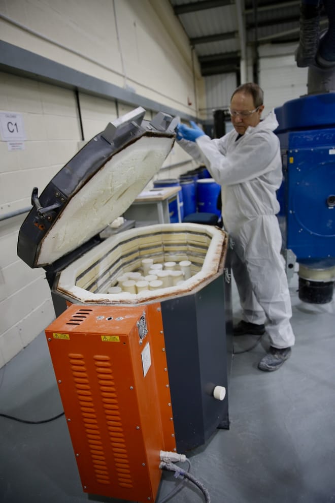 A person in protective gear opens a kiln filled with tubes.