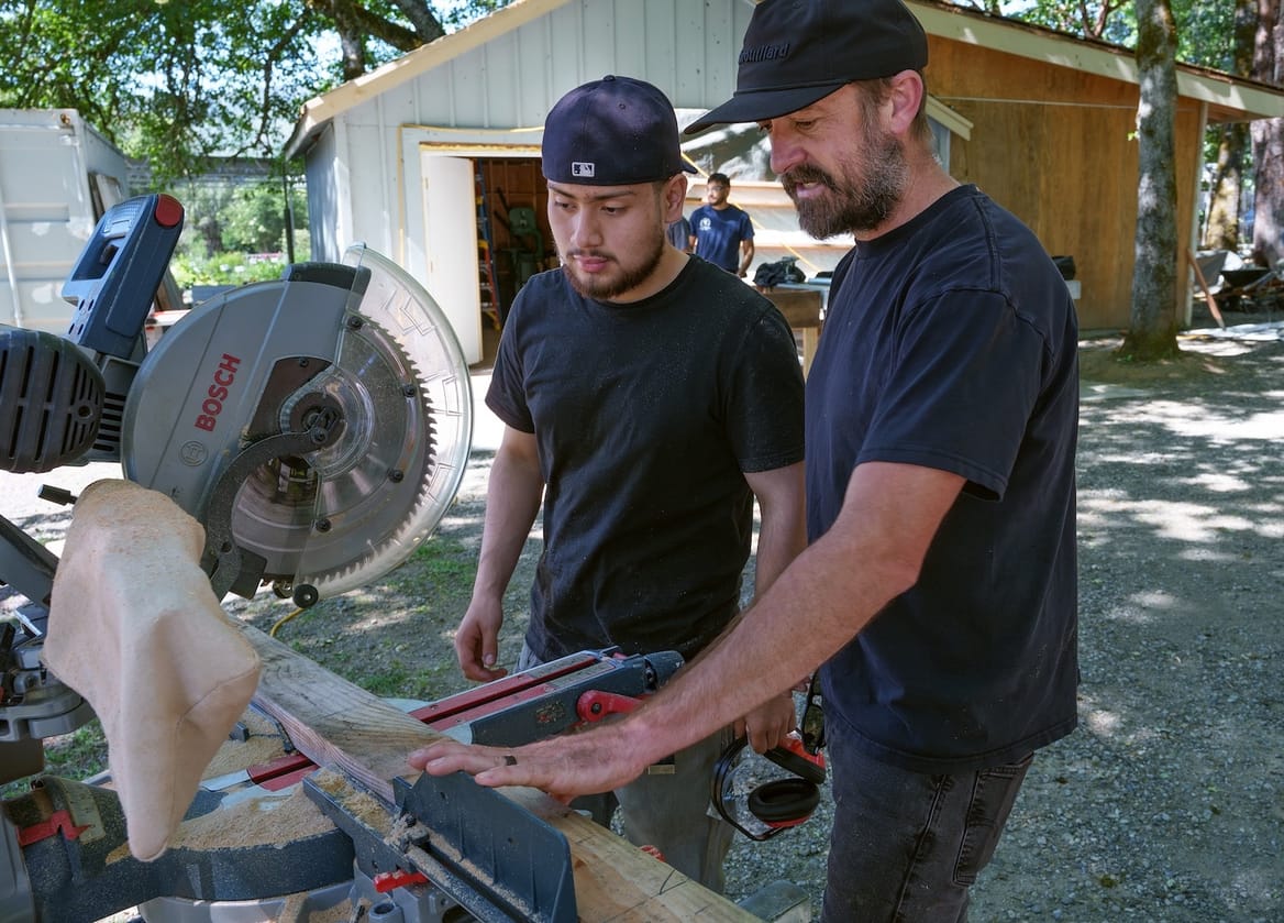 Two people use a round saw outside.