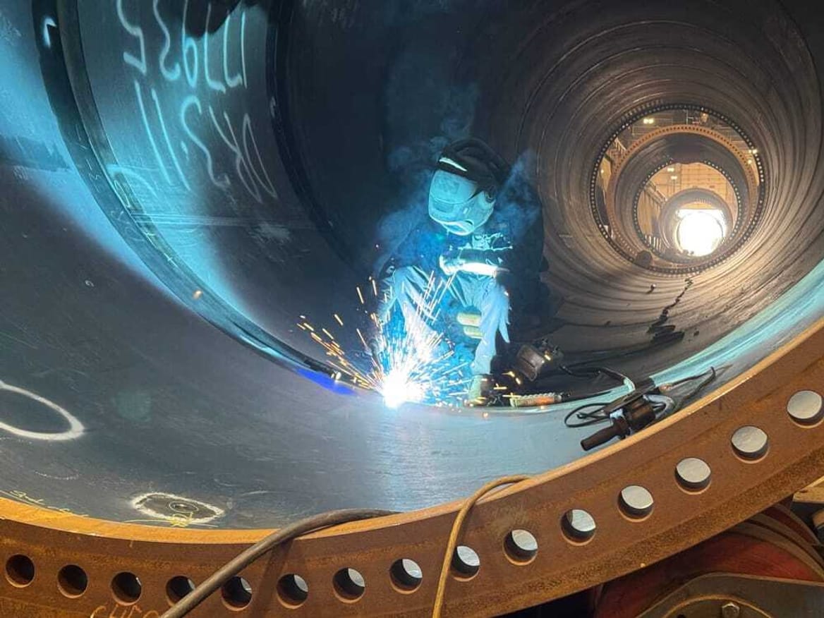 Sparks fly around a welder working inside a large metal tube
