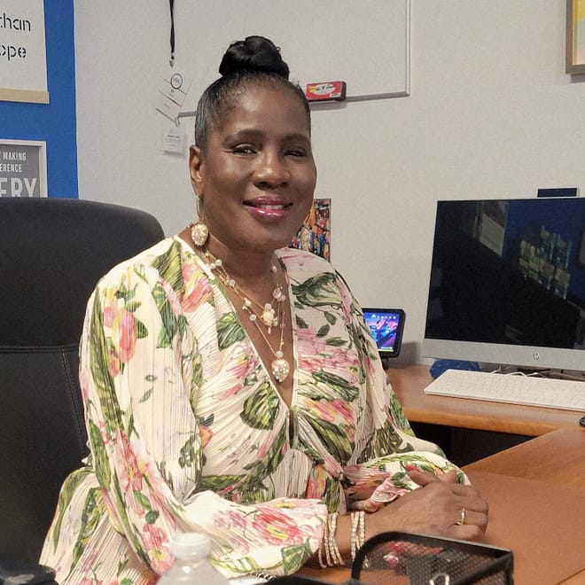 A woman in a blouse and jewelry sits at a desk with a computer on it