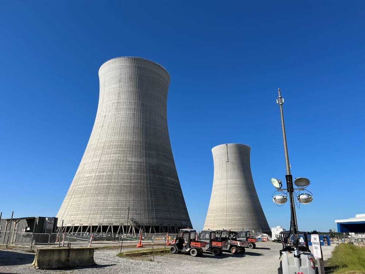 Two large, gray industrial structures rise against a blue sky.
