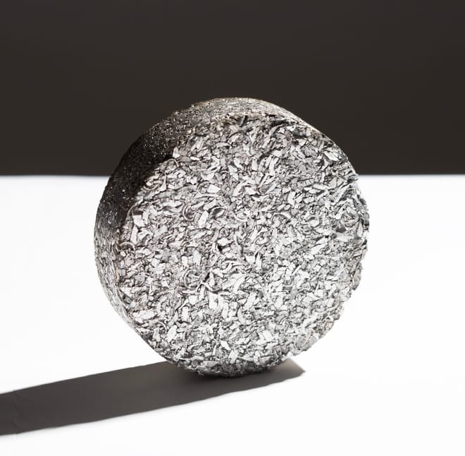 A silver-colored puck against a plain black and white background