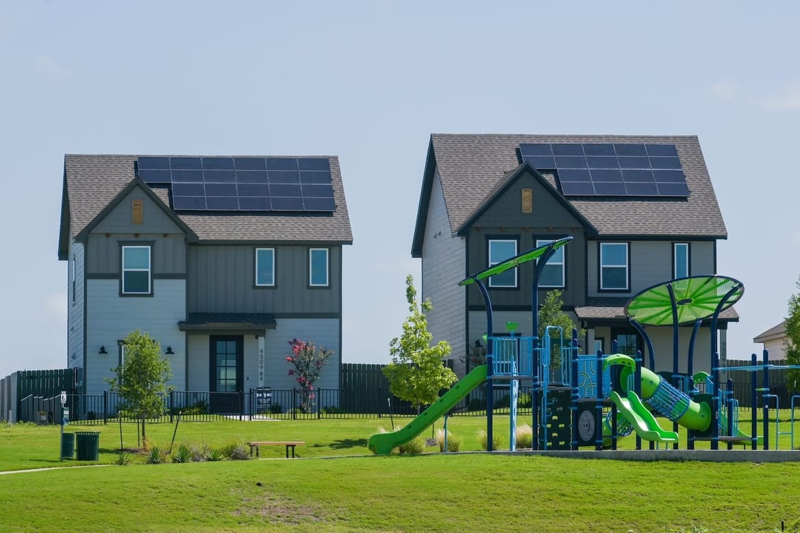 A playground on the grass in front of two homes with rooftop solar panels
