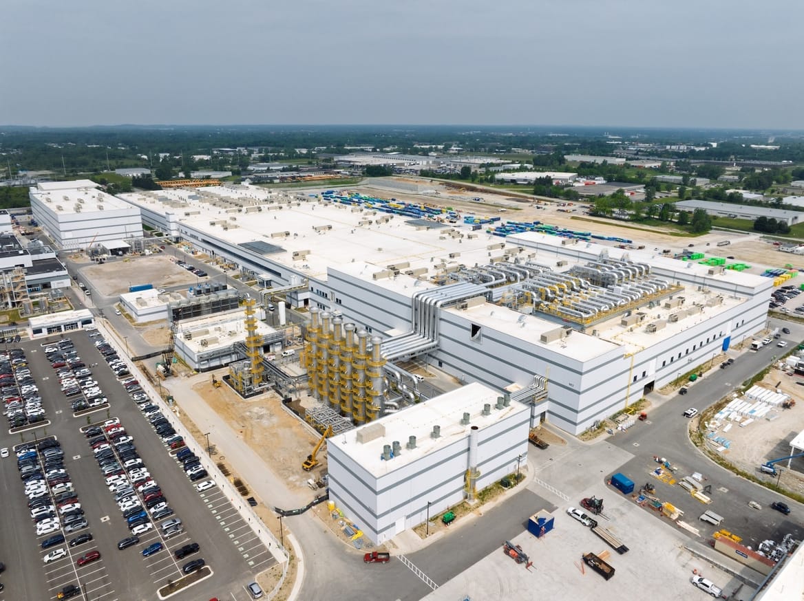 Aerial view of large white industrial manufacturing complex surrounded by parking lots
