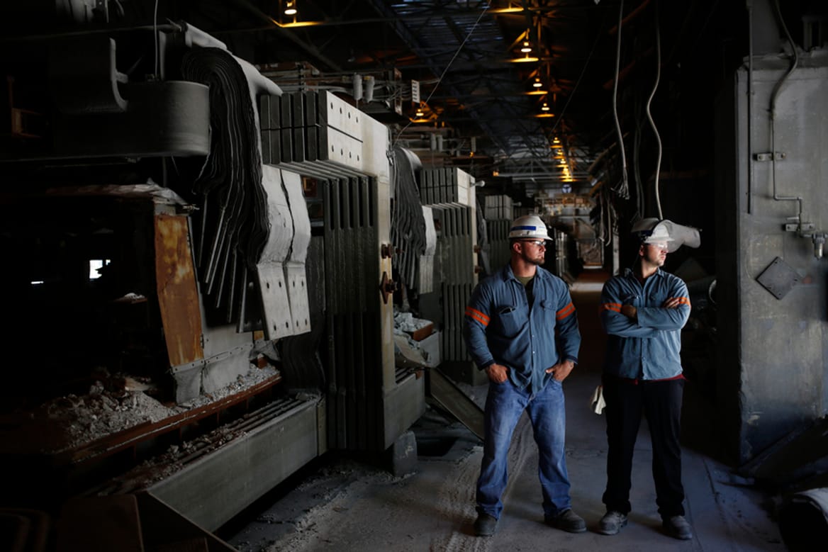 Two men in work gear and hard hats stand inside a factory