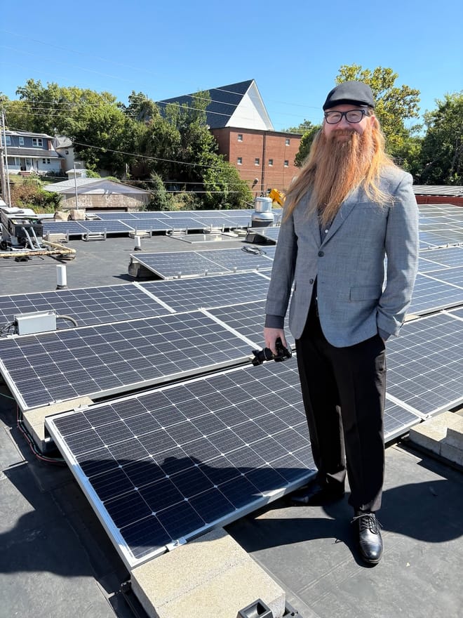A person stands on a roof next to a solar panel