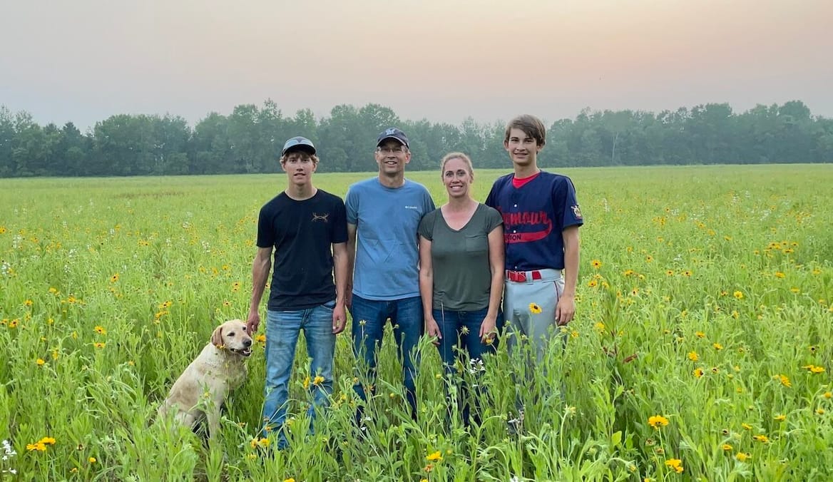 Family of four and a dog stand in a field of wildflowers