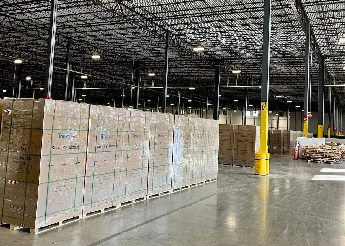 Boxes stamped with "Trinity Solar" and stacked on a gray warehouse floor