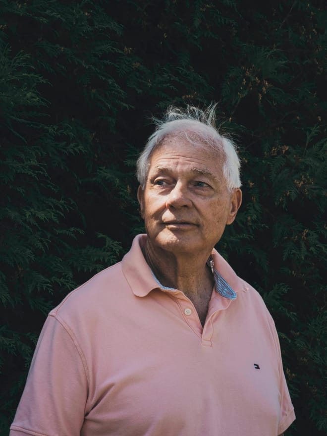 Man with white hair wearing a light-pink shirt