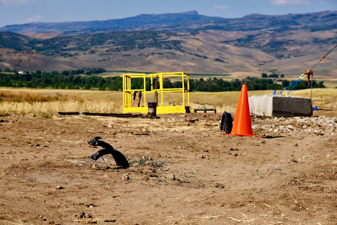 Two flexible ends of black pipe stick out of sandy brown soil at Hayden's geothermal drilling site.