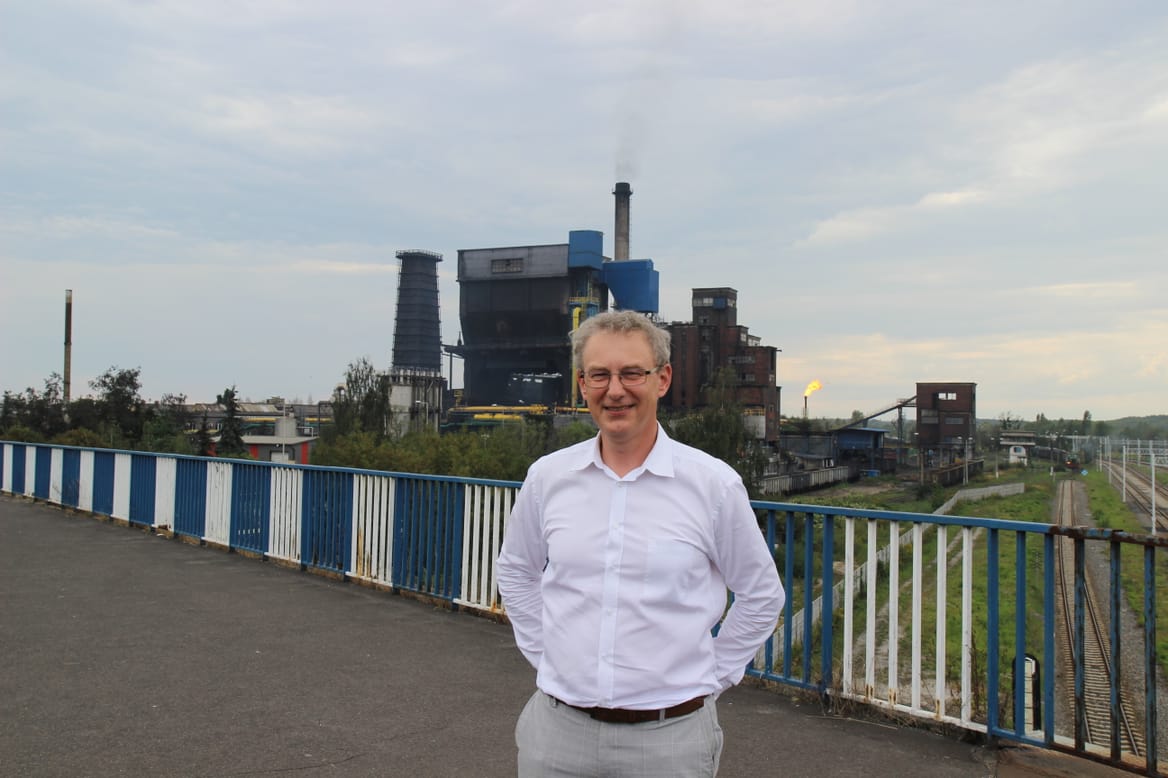 Man on bridge in front of the towers and buildings of the coking plant against a gray sky