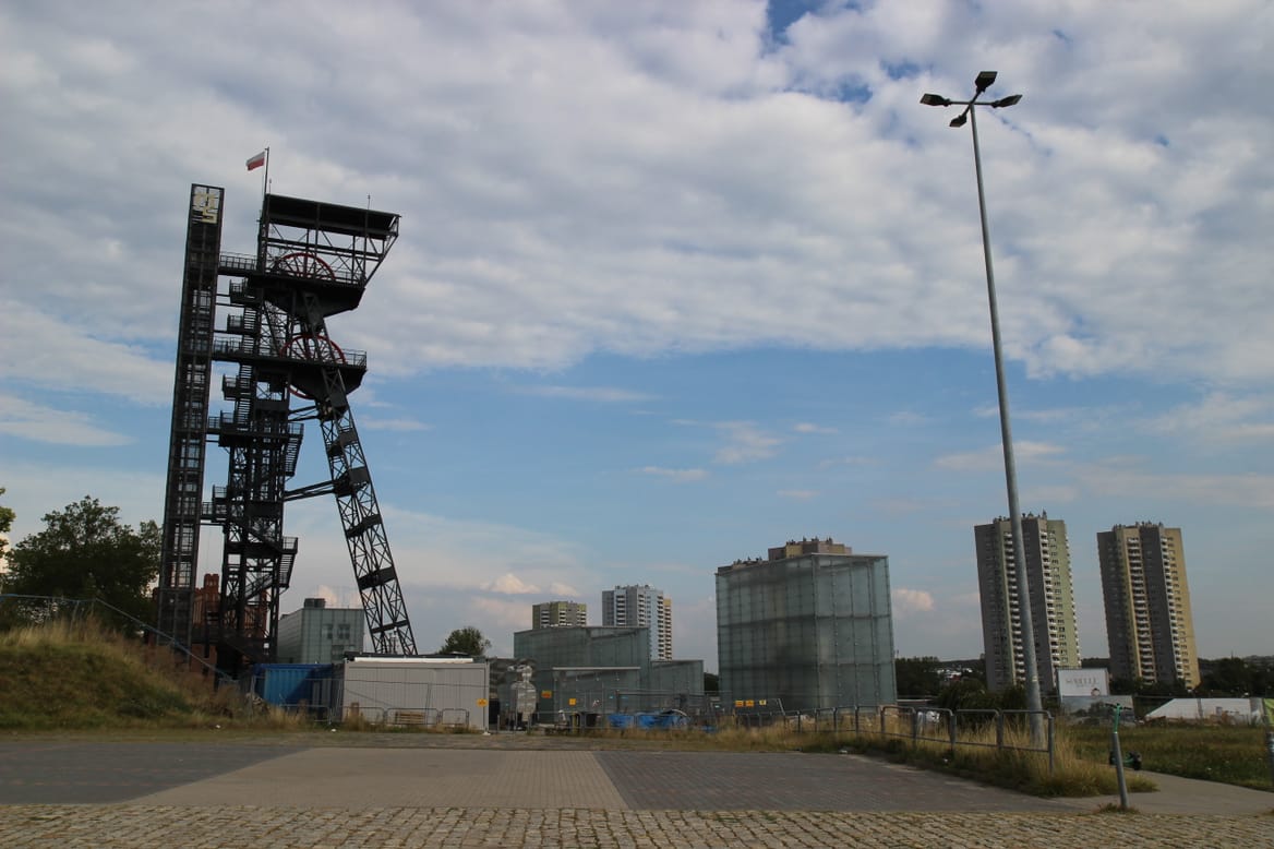 flat plaza, apartment buildings, and other buildings in the distance, and a tall, old, rusted structure