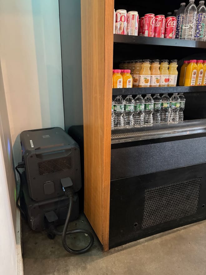 A black battery next to a refrigerated case with water, juice, and Coke cans