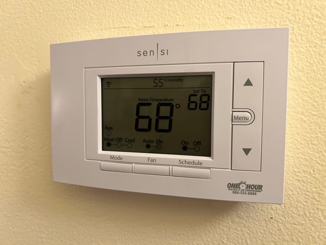 Close-up of a thermostat at 68 degrees on a yellow wall