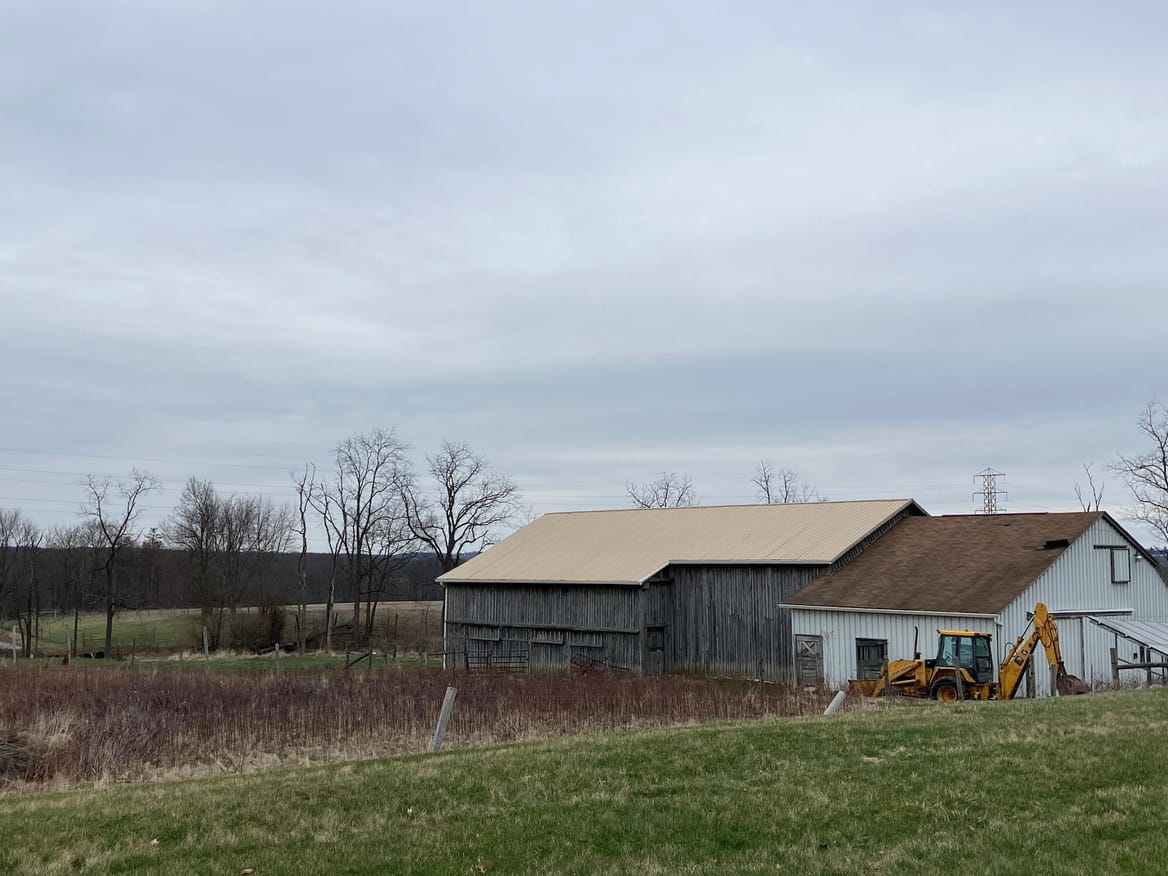 Two barn structures, one wood, one white and a backhoe