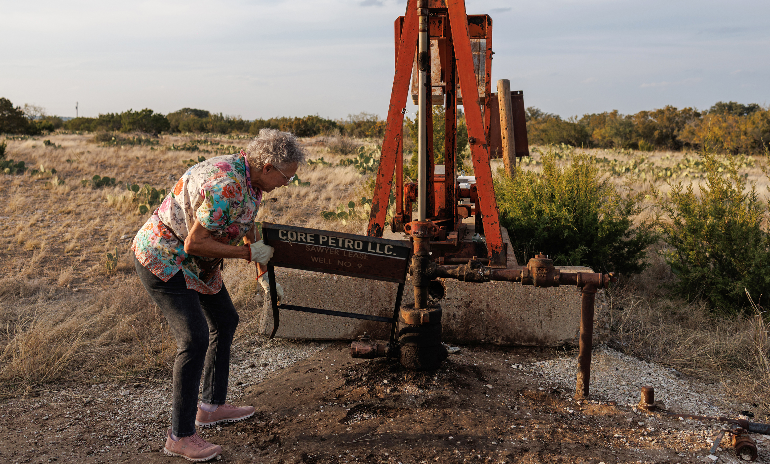 Jackie Chesnutt props up a sign next to a leaking oil well operated by CORE Petro on her property near Knickerbocker, Texas, on Nov. 18, 2025.