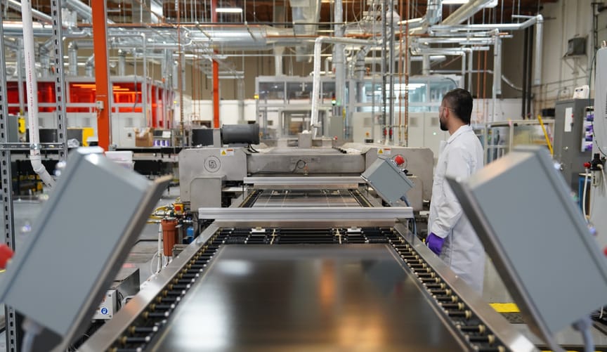 Conveyor belt in a factory with a white-lab-coated worker facing away from the camer