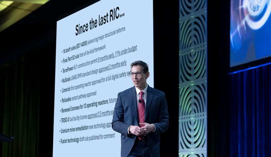 Man in suit and red tie onstage in front of a projection reading "Since the last RIC..."