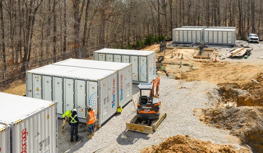 Plot with battery containers and construction equipment surrounded by woods
