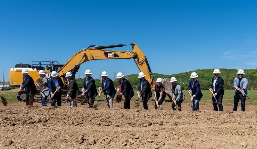 13 people in hard hats shoveling dirt on a construction site