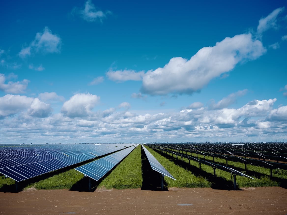 Rows of solar panels under a blue sky with a few clouds