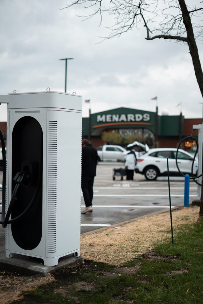 White charging port in a parking lot with Menard's store sign in background